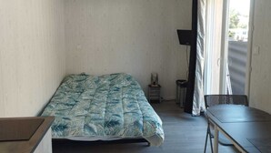 A small, sparsely furnished room with a bed, a table, and a chair.