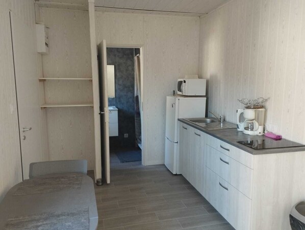 Una cocina compacta con armarios blancos, una encimera, microondas, nevera y cafetera.