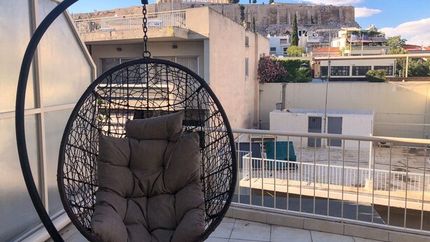 Uma cadeira suspensa numa varanda com vista para um edifício histórico ao fundo.