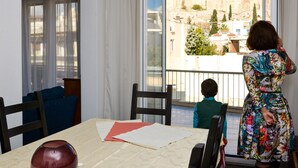 Quarto com uma mesa de jantar, cadeiras, um vaso e vista para a cidade através de uma janela.