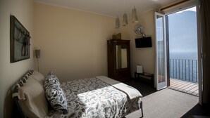 A bedroom with a bed, a dresser, a mirror, and a balcony with a view of the sea. - La Darsena di Riva Grande - Comballi (montrasio)