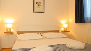 Ein Hotelzimmer mit einem Bett, zwei Nachttischlampen, einem gerahmten Kunstwerk an der Wand und einem Fenster mit Vorhängen.