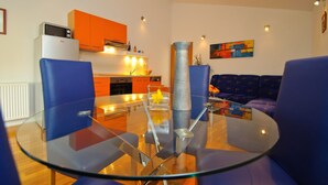 Ein modernes Wohnzimmer mit einem Glastisch, blauen Stühlen, einer Couch und einer Küche im Hintergrund.