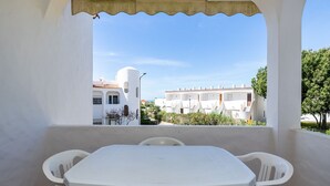 Un balcon avec une table et des chaises blanches, donnant sur une rangée de bâtiments blancs, eux aussi dotés de balcons.