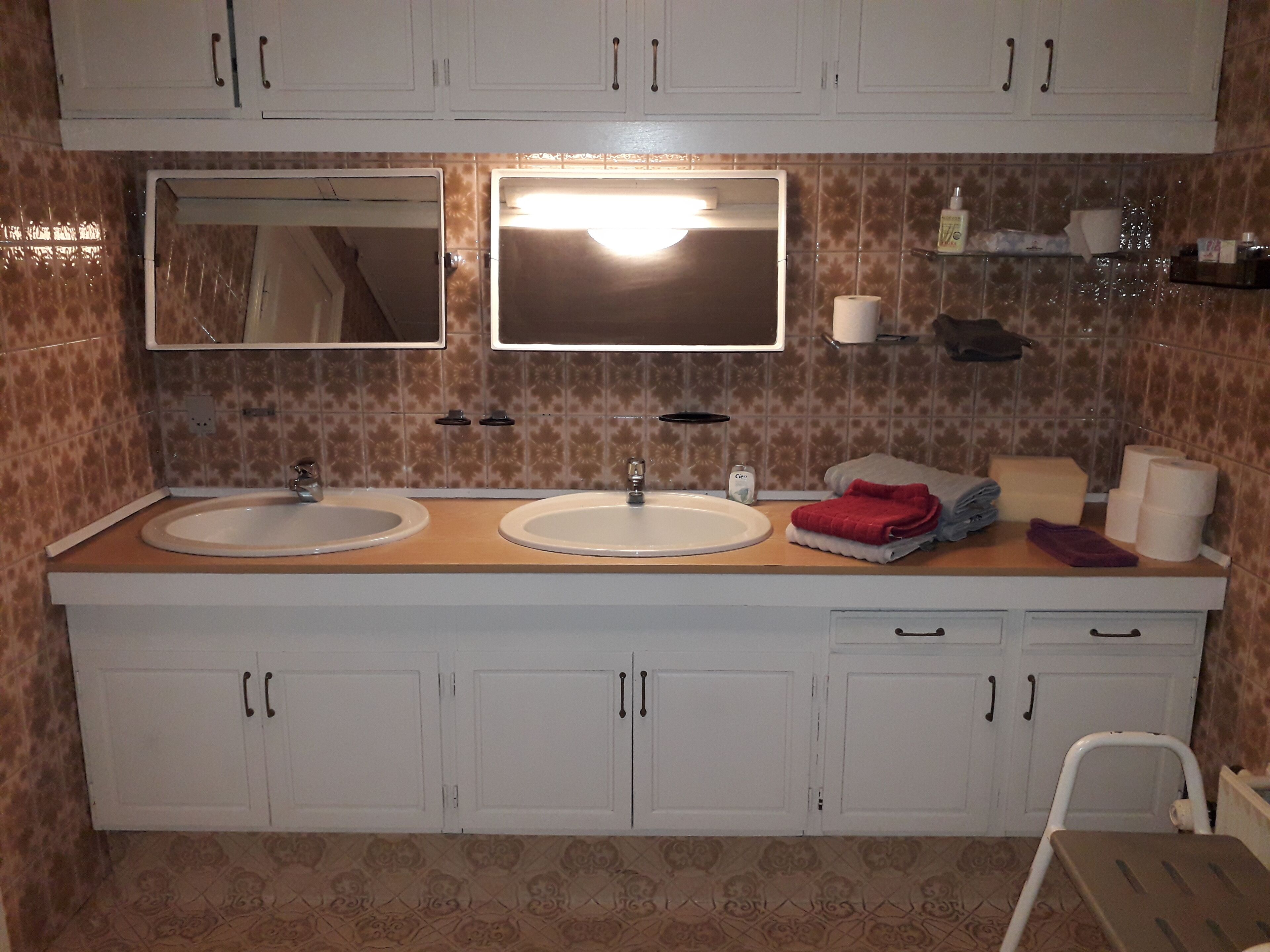 A bathroom with two sinks, a mirror, and a vanity with cabinets.