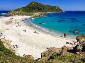 Une plage aux eaux turquoise et limpides, bordée de sable fin, avec une colline rocheuse en arrière-plan.