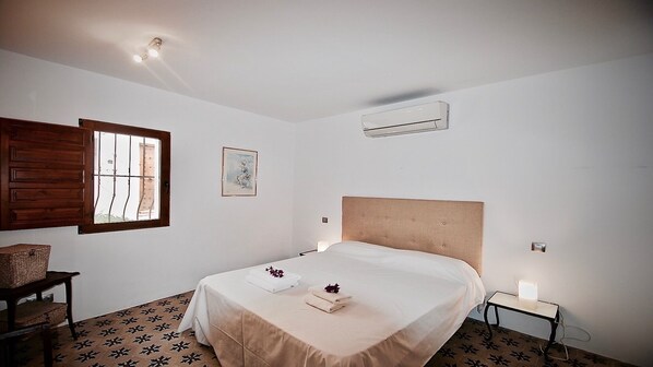 A bedroom with a bed, a window with wooden shutters, an air conditioning unit, a bedside table with a lamp, and a small chair. - House in the privileged area of the old town Altea (Altea)