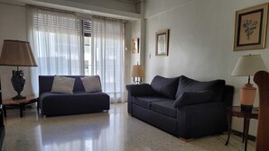 Uma sala de estar com dois sofás escuros, uma mesa de centro e duas luminárias. Há duas molduras com quadros na parede.