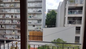 Um edifício residencial com vários andares, varandas, aparelhos de ar condicionado e vista para uma árvore e um jardim.