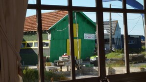 Visão pela janela mostrando um prédio verde, uma porta amarela e uma placa em idioma estrangeiro.