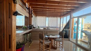 A spacious room with a high ceiling, wooden beams, a dining area with a round table and chairs, and large windows offering a view of the outside. - Charming 2 bedroom  Penthouse with nautical decor (Aradir Provence)