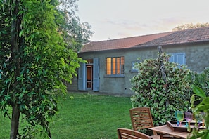 A rustic house with a tiled roof, a wooden door, and a small garden with a wooden table and chairs.