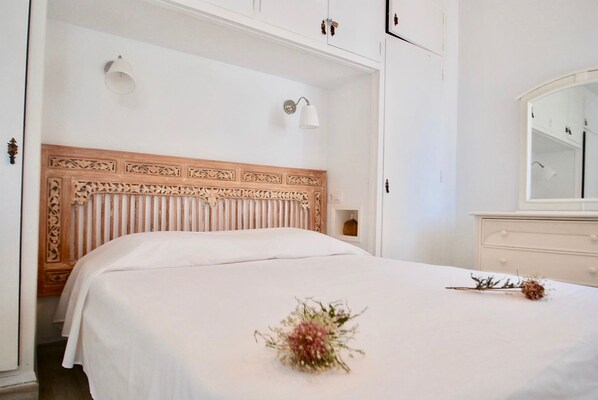 A bedroom with a wooden headboard, a white bedspread, a bedside table, and a mirror on the wall. - Le Paradis d'Atenea (Altea)