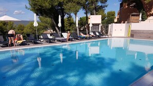 Una piscina con sillas de descanso y sombrillas, rodeada de árboles y edificios.
