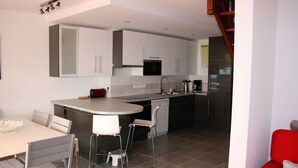 Una cocina moderna con armarios blancos, un horno negro y un lavamanos de acero inoxidable. Hay una zona de comedor con una mesa y sillas blancas.