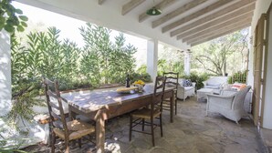 Un espacio comedor al aire libre techado, con una mesa de madera, sillas y un sofá de mimbre.