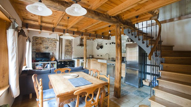 Ein rustikales Interieur mit einem Holzesstisch, Stühlen, einer Couch, einer Küche mit Steinwand und einer Holztreppe.