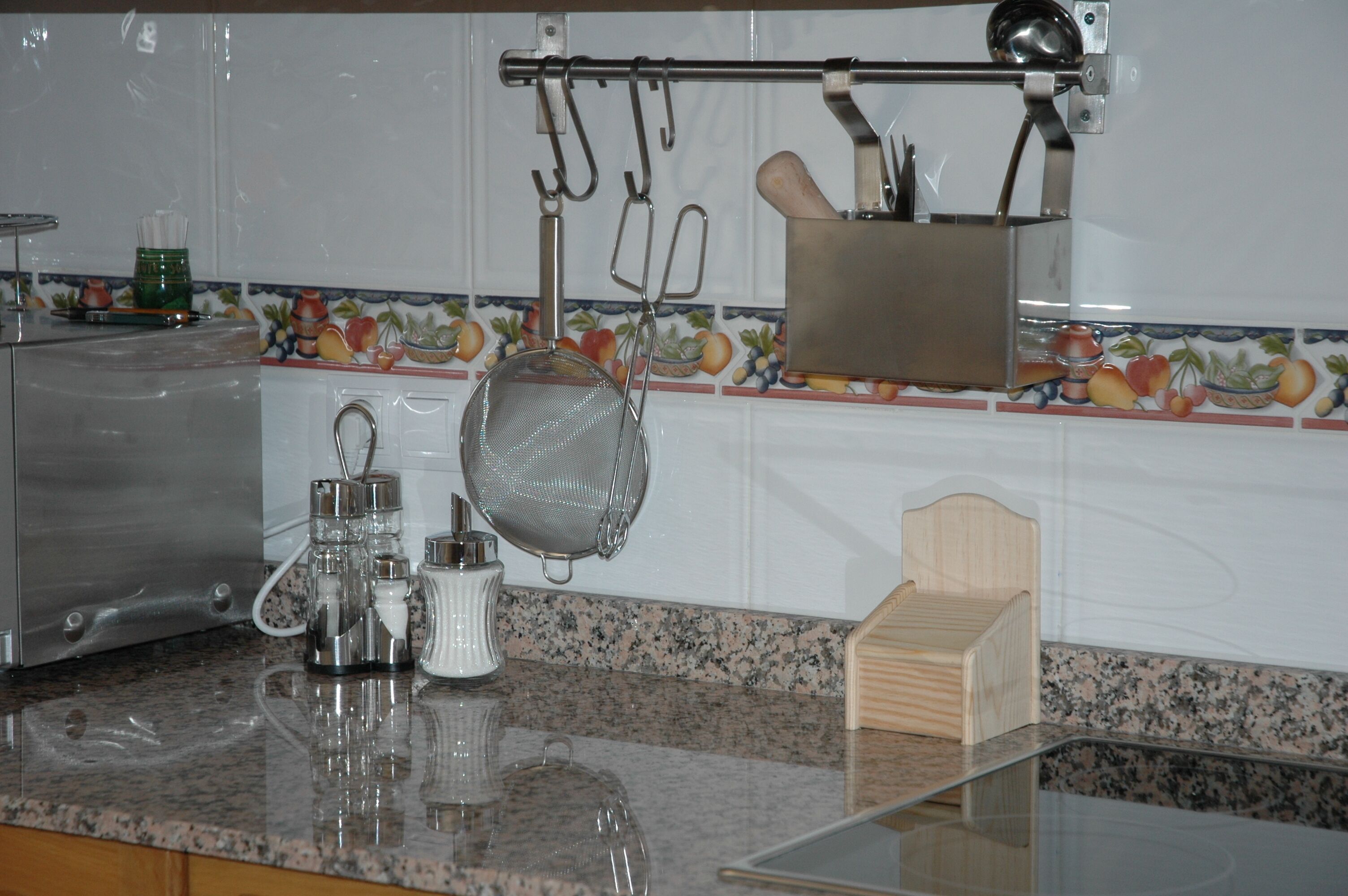 A kitchen with granite countertops, a coffee maker, a strainer, and hanging utensils.