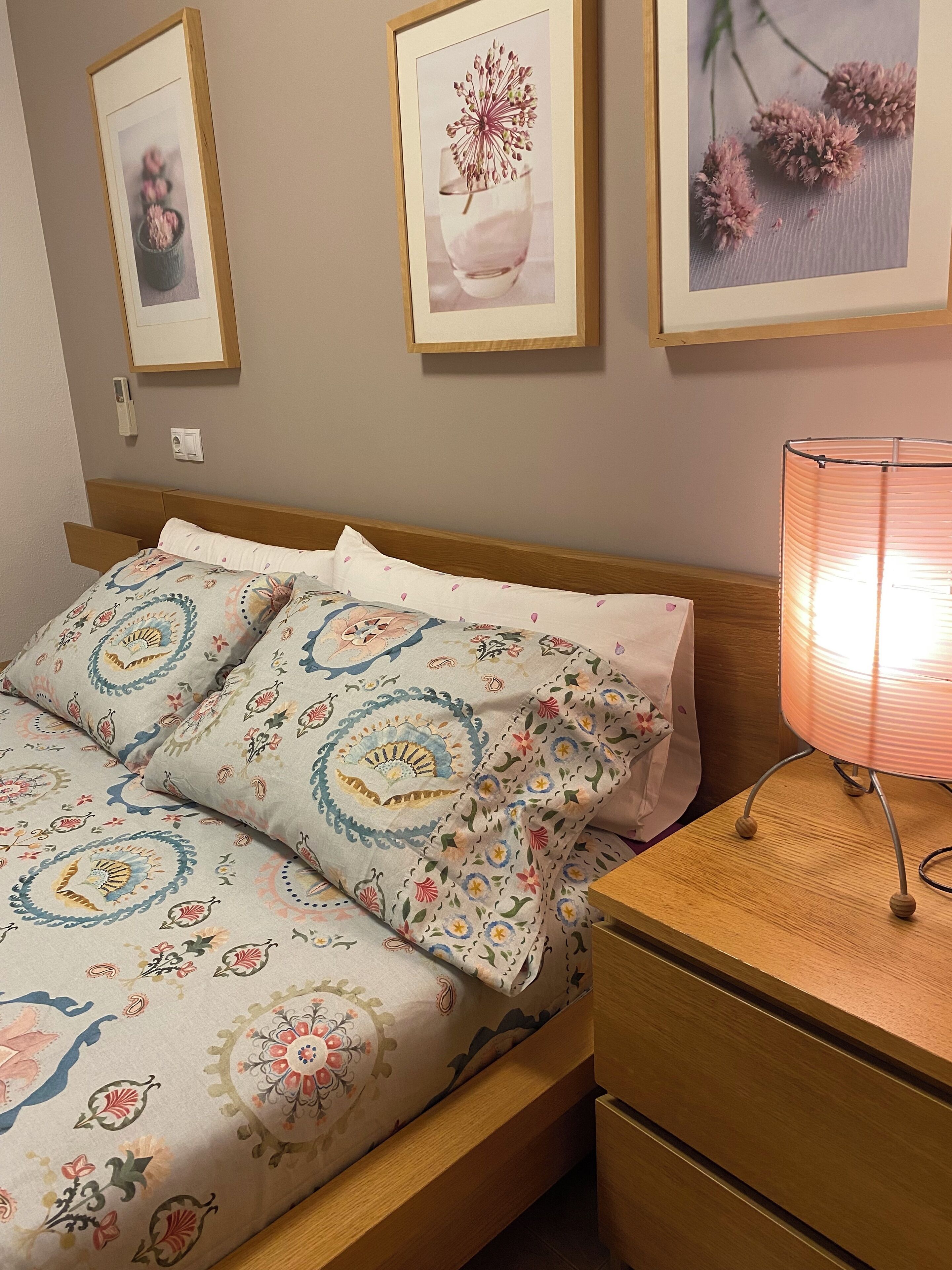 A neatly made bed with floral bedding, a bedside lamp, and framed pictures on the wall.