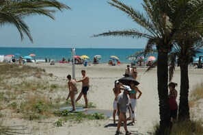 A beach scene with people, umbrellas, and palm trees.
