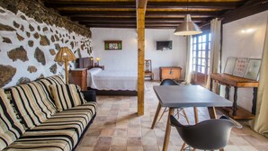 Une pièce chaleureuse avec un mur en pierre, des poutres apparentes, un lit, un canapé, une table à manger et un téléviseur.