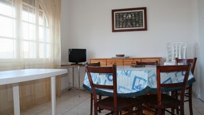 A dining area with a table and chairs, a television, and a framed picture on the wall. - Rents T3 - Leucate beach - Ground floor - Beachfront (Leucate)