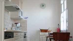 A kitchen with white cabinets, a clock, a window, and a chair. - Rents T3 - Leucate beach - Ground floor - Beachfront (Leucate)