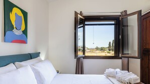 Una habitación de hotel con cama, almohadas, un ventanal con vistas y un cuadro en la pared.