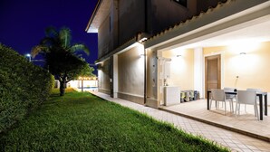 Un patio exterior bien iluminado con una mesa y sillas de comedor, un espacio de estar cubierto y un césped cuidado.