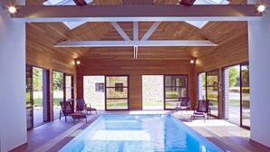 Ein moderner Innenpool mit klaren Glaswänden, Holzbalken an der Decke und einer Steinwand im Hintergrund.