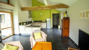 Eine moderne Küche mit grüner Akzentwand, einem Holzbalken an der Decke und einem Essbereich mit Sofa und Tisch.