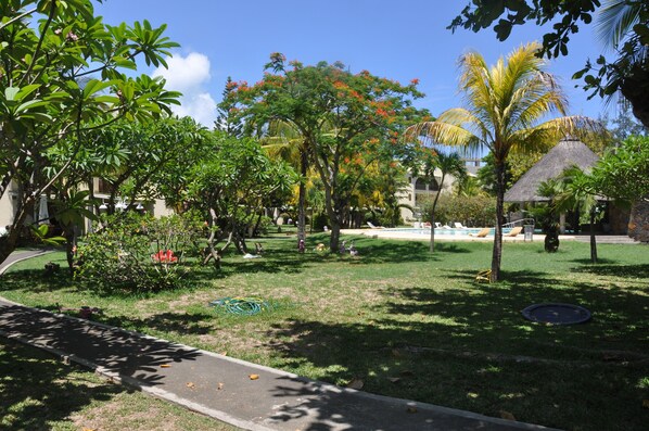 A lush garden with a pool, palm trees, and a thatched-roof structure. - Bain Boeuf Pereybere: Residential flat (Bain Boeuf (Péreybère))