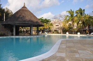 A swimming pool with a thatched-roof pavilion, lounge chairs, and palm trees. - Bain Boeuf Pereybere: Residential flat (Bain Boeuf (Péreybère))