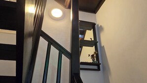 Eine Wendeltreppe mit Oberlicht, die zu einem Balkon führt, eine runde Leuchte und ein kleines Regal mit einer Vase.