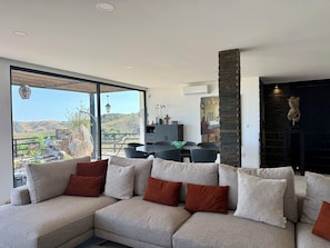 Un salon moderne doté d’un canapé d’angle, d’un coin repas et offrant une vue sur un paysage montagneux.