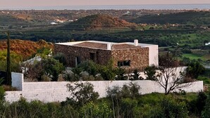 A stone building with a flat roof, surrounded by greenery and a view of a distant landscape.