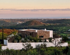 A stone building with a flat roof, surrounded by greenery and a view of a distant landscape.