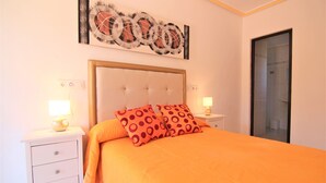 Une chambre à coucher avec un grand lit, deux tables de chevet, une petite table et une œuvre d’art accrochée au mur.