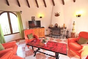 Un salon avec un sol à carreaux, deux fauteuils orange, une table rouge, une cheminée et un téléviseur.