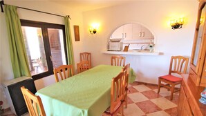 A dining area with a table covered in a green tablecloth, wooden chairs, a small refrigerator, and a kitchen area with cabinets and a microwave. - MARYVILLA0231-Wifi y Parking Gratis-Cerca Playa (Calpe)