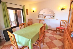 Un coin repas avec une table recouverte d’une nappe verte, des chaises en bois, un petit réfrigérateur et un espace cuisine équipé de placards et d’un four à micro-ondes.