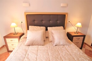 Ein ordentlich bezogenes Bett mit einer gepolsterten Kopfteil, zwei Nachttische mit Lampen und eine kleine Kommode.