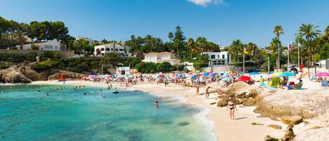 A beach with clear turquoise water, sandy shore, and buildings in the background.