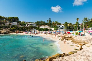 Une plage avec une eau turquoise et limpide, des gens qui se baignent et des parasols.