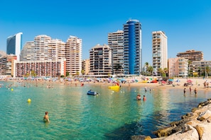 Un paysage urbain côtier avec de hauts immeubles, une plage de sable et une eau bleue et limpide.