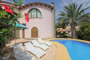 Ein Poolbereich mit Liegestühlen, einer Steinmauer und einem Gebäude mit Bogenfenstern und einer rosafarbenen Fassade.