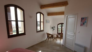 A bedroom with a large bed, two windows, a fan, and a door leading to another room.
