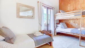 Quarto de cabana de madeira com uma cama beliche, uma cama de solteiro, uma janela com cortinas e um espelho na parede.