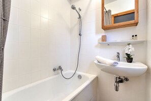 A bathroom with a white bathtub, a shower with a handheld hose, a sink with a mirror above it, and a small potted orchid. - Telemark Two. Perfect location in the centre of town. (Morzine)