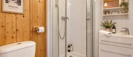 A bathroom with a wooden wall, a framed picture, a glass-enclosed shower, a toilet, and a sink with a mirror above it.
